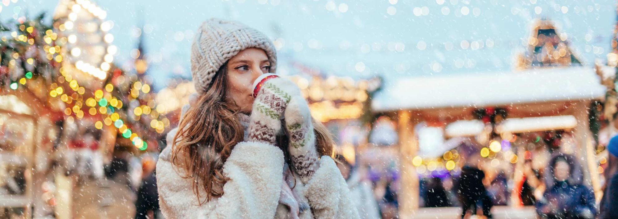 Frau wärmt sich auf dem Weihnachtsmarkt auf mit einer Tasse Glühwein